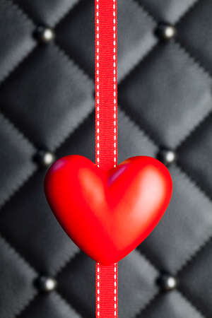Red heart and ribbon on black quilted leatherの写真素材