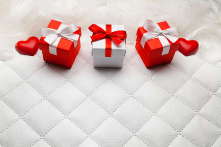 Three red gift boxes and red hearts on white leather backgroundの写真素材