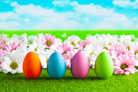 Easter eggs and colorful flowers on the grass and blue sky backgroundの写真素材