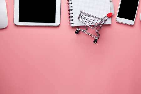 Mobile phone, shopping cart, tablet, computer keyboard, headphones and notebook on pink backgroundの写真素材