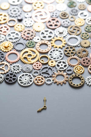 Small clock hands and many gears on a gray background