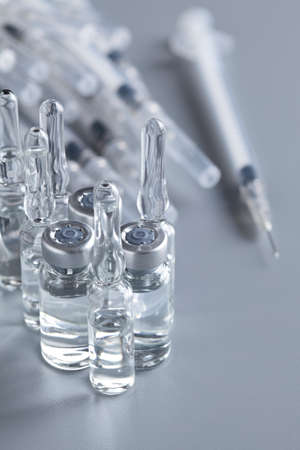 Liquid medicine in an ampoule and a syringe on a gray tableの写真素材