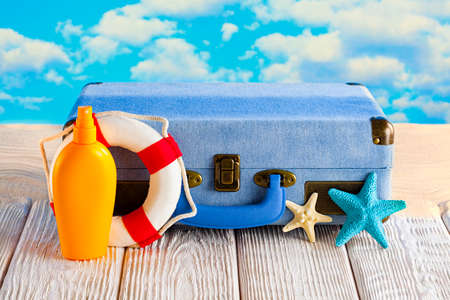 Summer holiday bag - tanning oil, lifebuoy and suitcase on wooden table and beach backgroundの写真素材