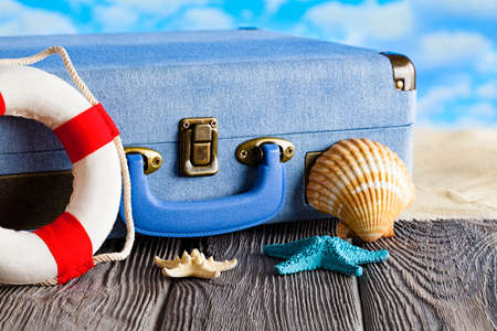 Holiday travel suitcase, lifebuoy and shells on wooden tableの写真素材