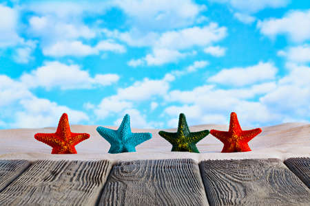 Four colorful starfishes on the beach sand and wooden table with empty spaceの写真素材