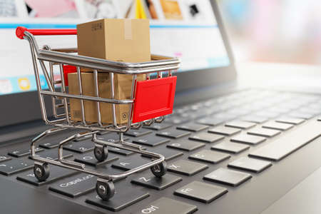 Shipping boxes in a grocery shopping cart on a laptop keyboard - 3d illustration as a symbol of online shopping and online storeの写真素材