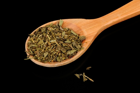 A pile of dried herbes de Provence (a mixture of dried herbs typical of Provence) in a wooden spoon against a black の写真素材