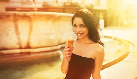 Beautiful girl with gelato smiling on sunny street. Young pretty woman having fun and eating ice...