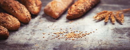 Fresh bakery food. Crusty loaves of mixed breads and buns and ears of wheat on rustic table...