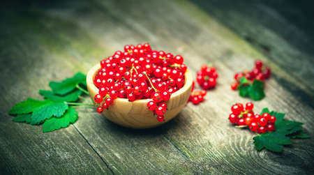 Fresh ripe red currant berries with leaves in a bowl on rustic old wooden table. Healthy organic...