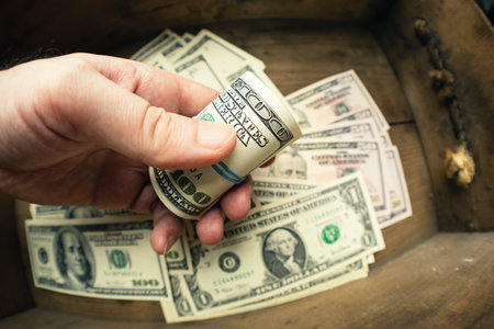 Hand holding one hundred US banknotes in roll over wooden drawer background with lot of dollars....