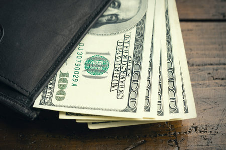 Leather wallet full of money on wooden table - one hundred US banknotes with president Franklin portrait. Cash of hundred dollar bills, paper currency background.の写真素材