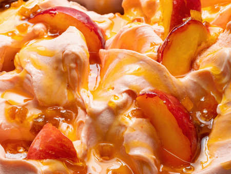 Frozen Peach flavour gelato - full frame detail. Close up of a beige surface texture of Ice cream covered with pieces of orange-red fruit.の写真素材