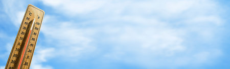 Wooden thermometer with red measuring liquid showing high temperature over 32 degrees Celsius on background of blue sky. Panorama. Concept of heat wave, warm weather, global warming, climate change.の写真素材