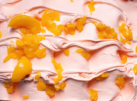Frozen Peach flavour gelato - full frame detail. Close up of a beige surface texture of Ice cream covered with pieces of orange color fruit.の写真素材