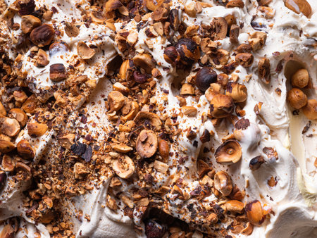 Frozen Hazelnut flavour gelato - full frame detail. Close up of a white creamy surface texture of Ice cream covered with pieces of nuts.の写真素材