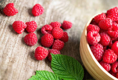 Fresh ripe red raspberries with leaves in a bowl on rustic old wooden table. Healthy organic food, summer vitamins, BIO viands, natural background. Copy space for your advertising text message.の写真素材
