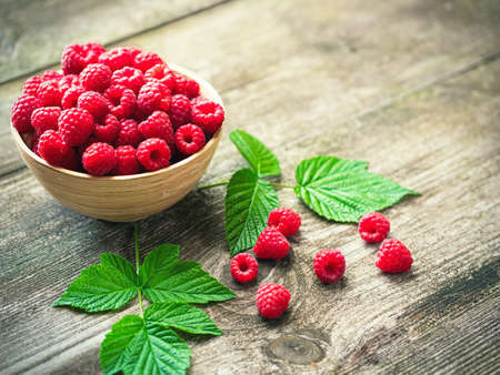 Fresh ripe red raspberries with leaves in a bowl on rustic old wooden table. Healthy organic food, summer vitamins, BIO viands, natural background. Copy space for your advertising text message.の写真素材