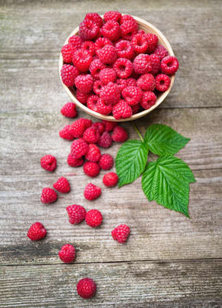 Fresh ripe red raspberries with leaves in a bowl on rustic old wooden table. Healthy organic food, summer vitamins, BIO viands, natural background. Copy space for your advertising text message.の写真素材