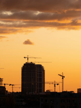 Silhouette of a skyscraper under construction process and cranes in the evening sky. New residential buildings being constructed.の写真素材