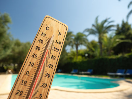 Wooden thermometer with red measuring liquid showing high temperatures on sunny day on background of swimming pool. Concept of vacation, holiday, warm weather and water cooling.の写真素材
