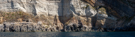 Weathered seaside rock face texture with parts of green and blue water. Aged volcanic stone wall surface background pattern with cracks and scratches. Banner. Ischia Island, Italy.の写真素材