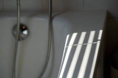 Thin lines of light on the wall. Shadow from the blinds. bathroom.