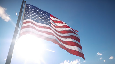 American flag waving in the wind against a blue sky with sun raysの素材