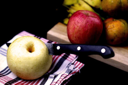 Image of a knife cutout the pear with apple, orange, banana in black backgroundの写真素材