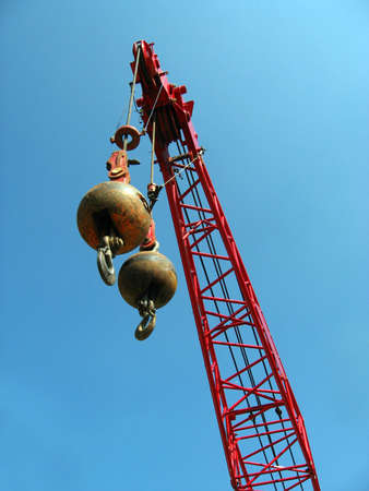 Two wrecking balls suspended from a red crane, high above the ground, against a blue sky background.の写真素材
