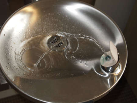 A stream of clean, clear water in a drinking fountain makes an arc from the spout to the drain の写真素材