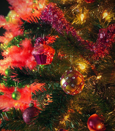 Closeup on a fashionable pink and gold sparkly Christmas ornament on a green tree, with pink tree and green ornaments in the background の写真素材