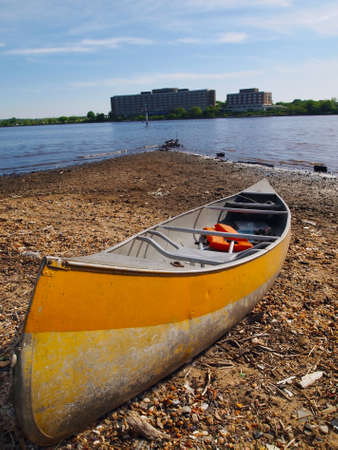 A yellow rowboat with a life preserver jacket sits in the late afternoon sun on a rocky point of land at the harbor の写真素材