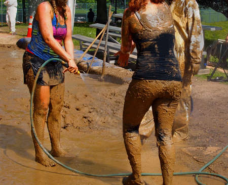 A group of young people hose mud of their bodies with cold water on a hot day in the sunshine. の写真素材