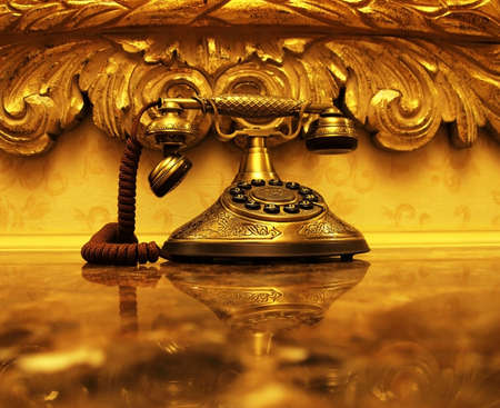 An antique gold telephone and reflection on a shiny marble desktop with vintage style wallpaper and picture frame in the background の写真素材