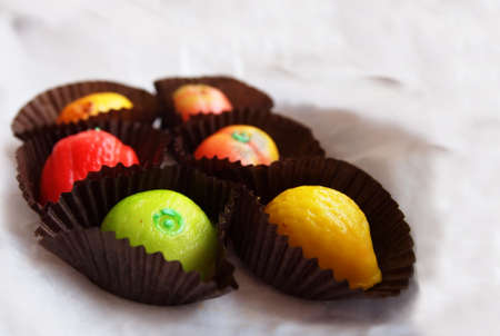 Six colorful pieces of marzipan fruit shapes in white tissue paper の写真素材