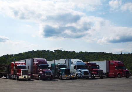 Six  big rig  tractor trailer trucks are parked in a row at mountain top truck stop の写真素材
