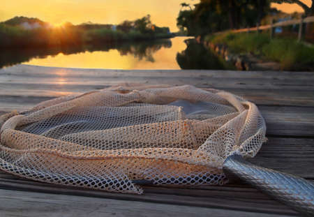 A pole style crab net lies on a dock over a river at sunset.