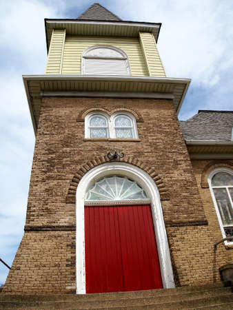 Vibrant red doors and round top stained glass windows in the brick facade of an old church.の写真素材