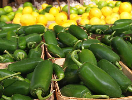 Baskets of fresh, hot, green jalapeno peppers for sale at a  local farmer's market with citrus fruits in the background.の写真素材
