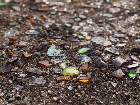 Jagged pieces of green, amber, brown, and clear broken glass on the ground with dirt in the...
