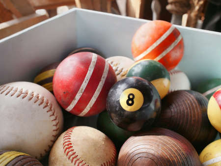 An old eightball in wooden bin full of vintage game balls, including pool, croquet, and baseball.の写真素材