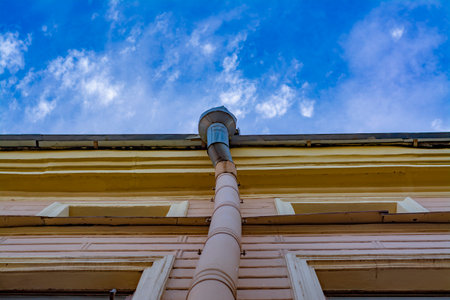Drainpipe on the wall of an old house on a background of blue sky