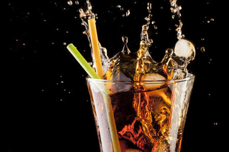 fresh cola juice and ice cubes splash in a glass on black backgroundの写真素材