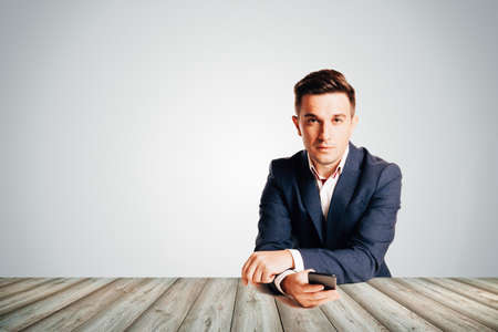 Attractive businessman in trendy suit sitting at desk against empty backgroundの写真素材