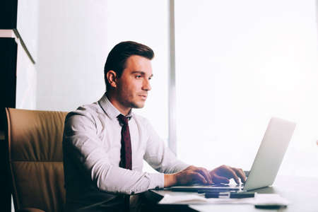 Attractive business man in smart casual wear sitting at his working place in officeの写真素材