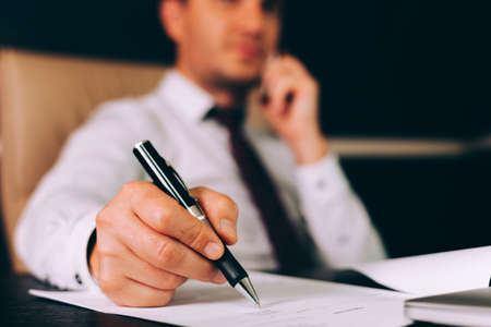 Attractive business man in smart casual wear sitting at his working place in office holding a smart...