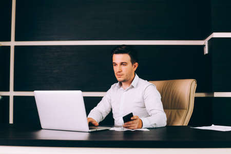 Attractive business man in smart casual wear sitting at his working place in office