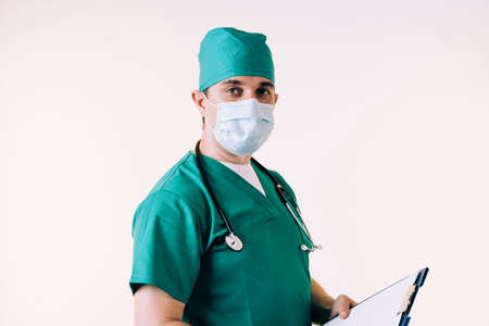 Young male doctor in uniform holding a clipboard posing in studio