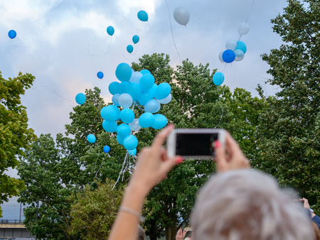 Helium balloons fly into sky and woman is photographing it with a mobile phoneの写真素材